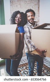 Smiling Young Black African Couple Moving Boxes Into New Home Together And Making A Successful Life.Cheerful Family Standing In Empty New Apartment.Vertical.Blurred Background.Cropped