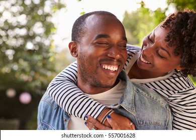 Smiling young black couple piggyback in garden, eyes closed - Powered by Shutterstock