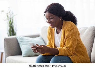 Smiling Young Black Lady Sitting On Couch At Home, Using Smartphone, Chatting With Her Friends Or Lover, Panorama With Copy Space. Happy African American Woman Holding Mobile Phone