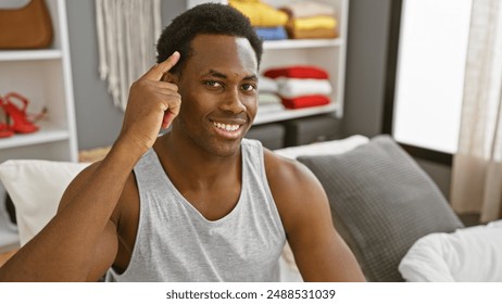 Smiling young black man pointing at his head, sitting in a casual bedroom interior filled with light. - Powered by Shutterstock