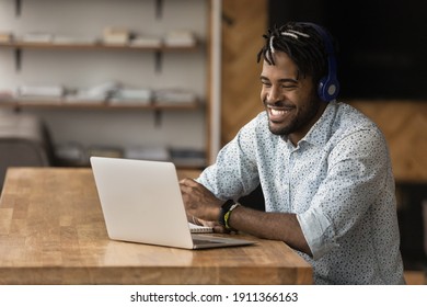 Smiling Young Black Man In Wireless Headset Take Part At Virtual Meeting With Friends Online Using Laptop. Laughing Millennial Afro Guy In Earphones Relax By Pc Screen Watch Funny Movie Video Content