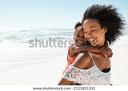Smiling young black mother and beautiful daughter having fun on the beach with copy space. Portrait of happy sister giving a piggyback ride to cute little girl at seaside. Lovely kid embracing her mom
