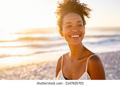 Smiling young black woman in beachwear enjoy sunset at beach. Satisfied beautiful girl with afro hair relaxing at beach during sunrise with copy space. African american woman daydreaming.