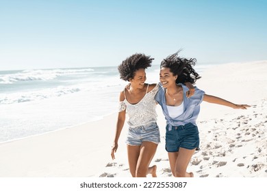 Smiling young black woman having fun at beach with her best friend. Latin hispanic young women running on seashore barefoot during vacation. Cheerful friends enjoying at sea on a bright sunny day. - Powered by Shutterstock