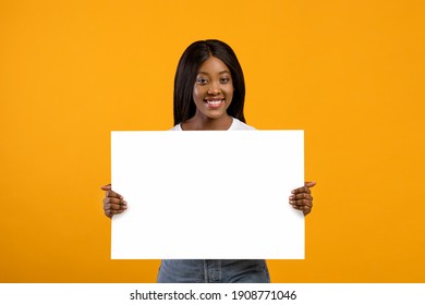 Smiling young black woman holding blank board for advertisement or text on yellow studio background. Pretty african american lady showing empty advertising placard, copy space