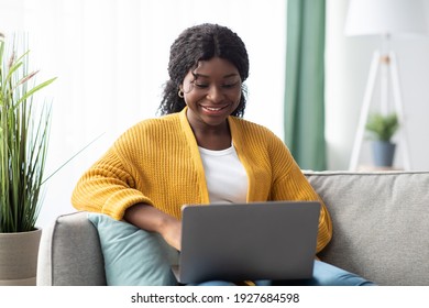 Smiling young black woman in knitted sweater freelancer working from home, sitting on couch, using laptop, copy space. Relaxed african american lady enjoying her weekend, surfing on internet on laptop - Shutterstock ID 1927684598