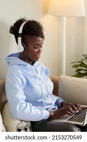 Smiling Young Black Woman Listening To Music In Headphones When Working On Laptop At Home