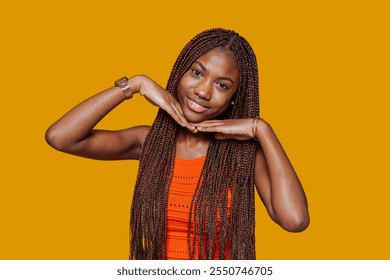 Smiling young black woman with long box braids framing her face with hands on a vibrant yellow background. - Powered by Shutterstock