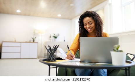 Smiling young black woman sitting at desk working on laptop taking notes in notebook, happy millennial female study watching webinar using computer writing check list, banner panorama, free copy space - Shutterstock ID 2101132870