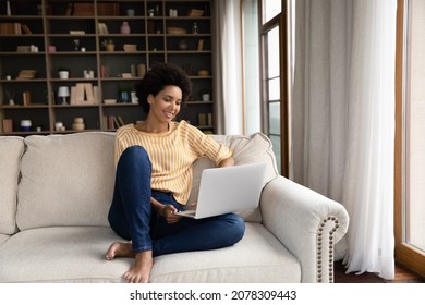 Smiling Young Black Woman Using Laptop Computer, Resting On Comfortable Couch, Talking On Video Call, Chatting Online, Browsing Internet, Watching Movie, Shopping On Internet. Lazy Digital Gadget User