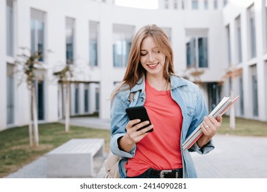 Smiling young blond female student using smart phone at university - Powered by Shutterstock