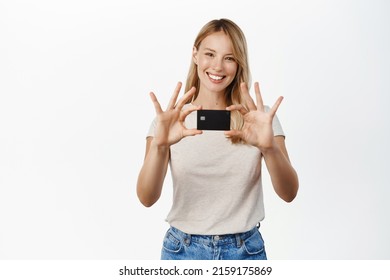 Smiling Young Blond Woman Showing Credit Card, Advertisement Of Bank, Contactless Payment, Standing In T-shirt Over White Background