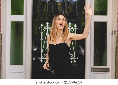 Smiling young blonde woman with braids waving with a friendly cheerful smile to her new neighbours. Girl leaves the house near green door and waving her hand. Girl wear black dress, meeting friends. - Powered by Shutterstock