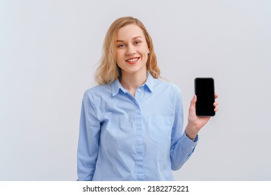 Smiling Young Blonde Woman Showing Mobile Phone Screen, Recommend Online Shopping Store. Indoor Studio Shot On White Background