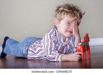 Smiling young boy covering his eye and playing with a swedish wooden horse