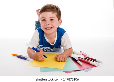Smiling young boy with felt pens writing and drawing on  colorful paper. White background.