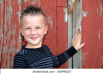 smiling young boy with spiky hair posing by an old red barn - Powered by Shutterstock