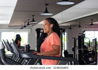 
Smiling young brazilian woman with braided hair orange t-shirt and headphones on gym mat