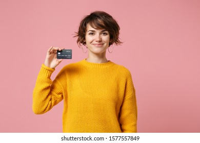 Smiling Young Brunette Woman Girl In Yellow Sweater Posing Isolated On Pastel Pink Wall Background Studio Portait. People Sincere Emotions Lifestyle Concept. Mock Up Copy Space. Hold Credit Bank Card