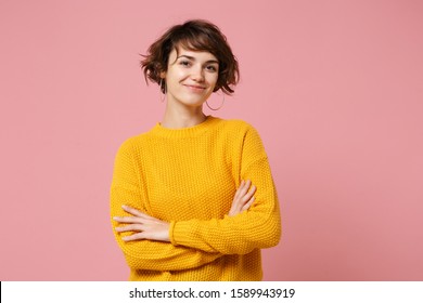 Smiling young brunette woman girl in yellow sweater posing isolated on pastel pink background studio portrait. People sincere emotions lifestyle concept. Mock up copy space. Holding hands crossed