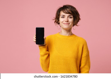 Smiling Young Brunette Woman Girl In Yellow Sweater Posing Isolated On Pastel Pink Background Studio Portait. People Lifestyle Concept. Mock Up Copy Space. Hold Mobile Phone With Blank Empty Screen