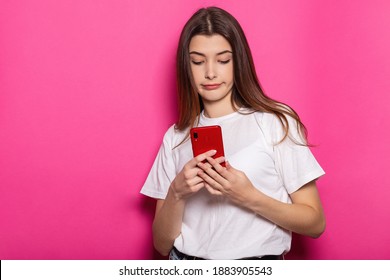 Smiling Young Brunette Woman Girl Posing Isolated On Pastel Pink Wall Background Studio Portait. People Lifestyle Concept. Mock Up Copy Space. Using Mobile Phone, Typing Sms Message