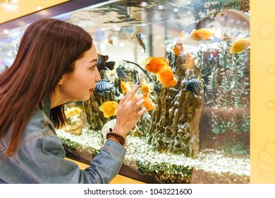 Smiling Young Brunette Woman Looking At Fish In Aquarium