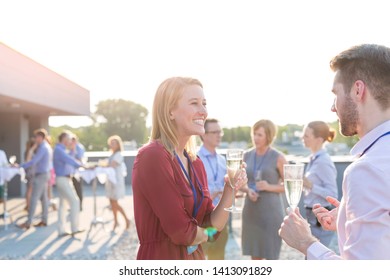 Smiling Young Business Colleagues Talking While Standing With Wineglasses At Rooftop Party