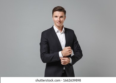 Smiling Young Business Man In Classic Black Suit Shirt Posing Isolated On Grey Wall Background Studio Portrait. Achievement Career Wealth Business Concept. Mock Up Copy Space. Straightening Sleeves