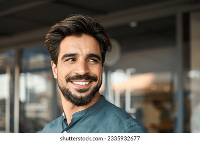 Smiling young business man standing looking away in office. Happy Latin businessman, male entrepreneur, professional manager or company employee worker close up portrait. Copy space - Powered by Shutterstock