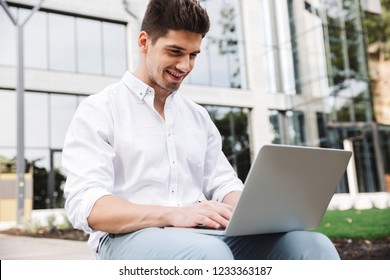 Smiling young business man working on laptop computer while sitting outdoors - Shutterstock ID 1233363187
