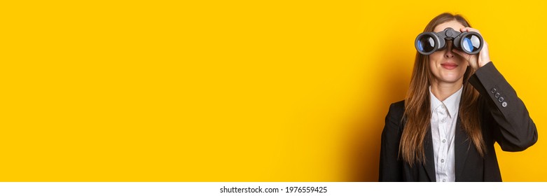 smiling young business woman looking through binoculars on yellow background.