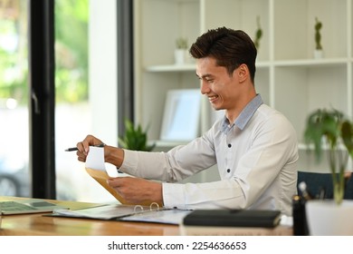 Smiling young businessman analyzing financial market and using laptop computer at his working desk - Shutterstock ID 2254636653