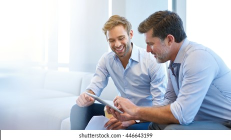 Smiling young businessman discussing something positive with his mature colleague, and using a digital tablet together - Powered by Shutterstock