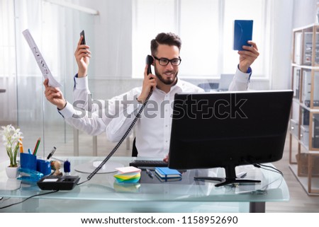 Smiling Young Businessman Doing Multitasking Work At Workplace