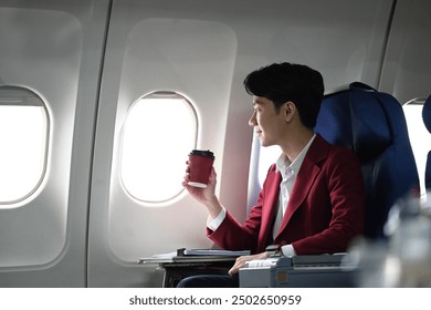 Smiling young businessman drinking coffee and enjoying the view through the aircraft window during the flight. - Powered by Shutterstock