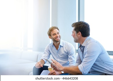 Smiling young businessman enjoying a positive conversation with a mature business partner in a modern space with large windows