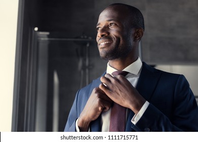 smiling young businessman putting on his tie at bathroom and looking away