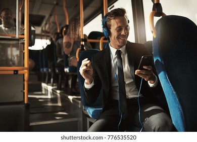 Smiling young businessman sitting on a bus during his morning commute snapping his fingers while listening to music on headphones  - Powered by Shutterstock