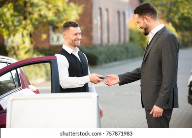 Smiling Young Businessman Standing Beside Car Getting Key From Valet