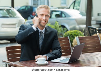 Smiling Young Businessman Talking On Cellphone Looking At Laptop