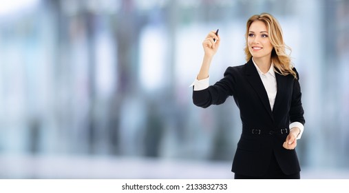 Smiling young businesswoman in black confident suit, writing or drawing on screen or transparent glass by marker, indoors. Blurred office background. Advertising sales deal offer. Save big concept. - Powered by Shutterstock