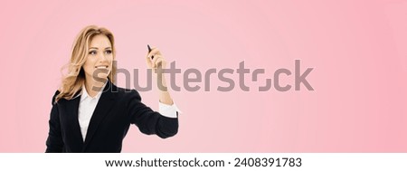 Smiling young businesswoman in black confident suit, writing or drawing on screen or transparent glass, by marker, isolated pink background. Wide banner composition image.