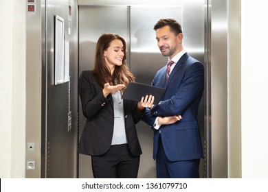 Smiling Young Businesswoman And Businessman Discussing While Using Digital Tablet Standing Near Elevator