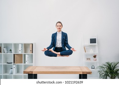 smiling young businesswoman with closed eyes meditating while levitating at workplace   - Powered by Shutterstock