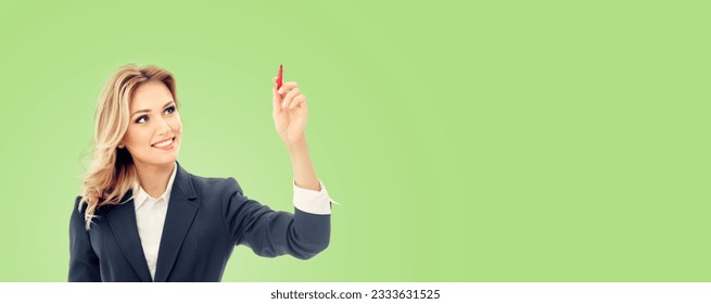 Smiling young businesswoman in grey confident suit, writing or drawing something on screen or transparent glass, by marker, isolated over light green color background.  - Powered by Shutterstock