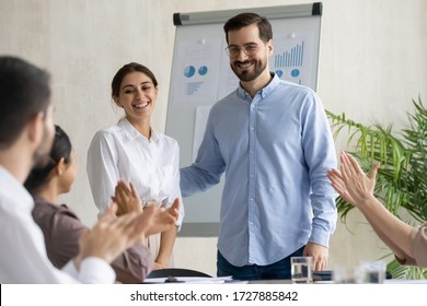 Smiling Young Businesswoman Takes Congratulations Clap Hands From Diverse Colleagues After Flip Charts Presentation In Boardroom At Company Meeting. Happy Auditor Standing In Front Of Board.