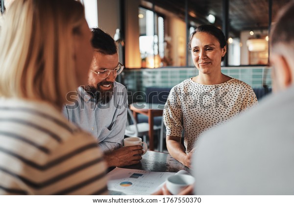 Smiling young businesswoman\
talking with a group of colleagues over coffee during their office\
break