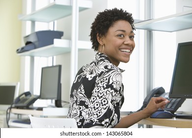 Smiling young businesswoman using computer at office desk