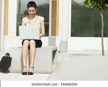 Smiling Young Businesswoman Using Laptop Outside Office